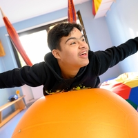 In Bethel Regional Haus am Funkturm in Dortmund wippt ein Junge lächelnd auf einer Hängeschaukel und stützt sich auf einem Gymnastikball ab, dabei hat er seine beiden Arme ausgebreitet