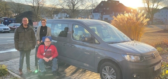 Ein Mann im Rollstuhl vor einem Auto, das von der Aktion Mensch gefördert wurde