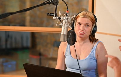 Eine Person bei der Gesangsaufnahme im Studio am Mikrofon