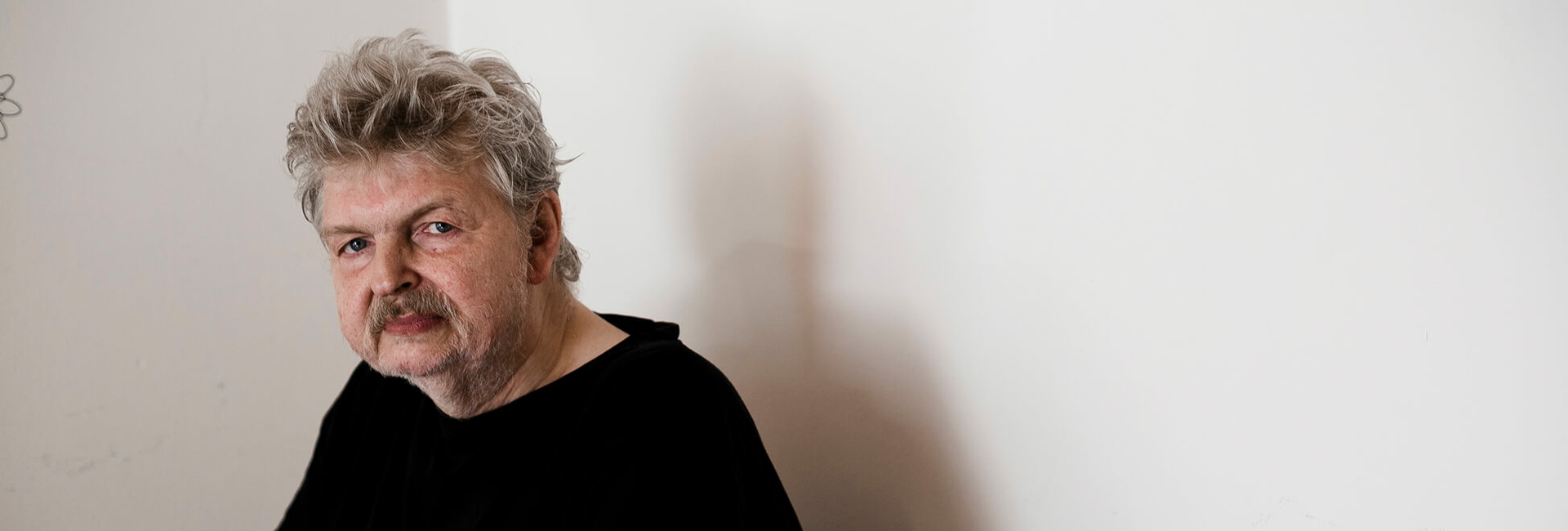 Älterer Mann sitzt vor einer Wand