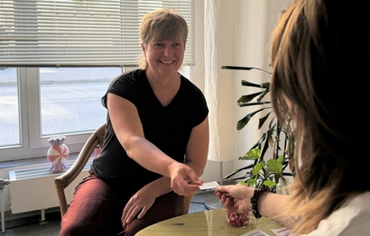 Zwei Frauen sitzen am Tisch der Frauenberatungsstelle von Bethel.regional. Eine Frau reicht der anderen eine Visitenkarte.