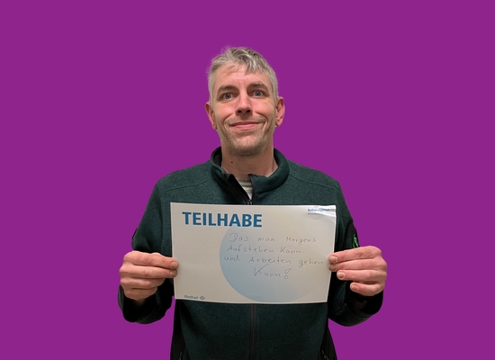 Mann mit Schild in der Hand Teilhabe Das man morgens aufstehen kann und arbeiten gehen kann.