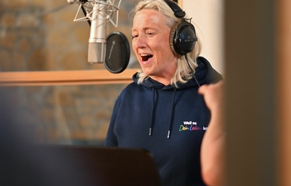 Eine Person bei der Gesangsaufnahme im Studio am Mikrofon