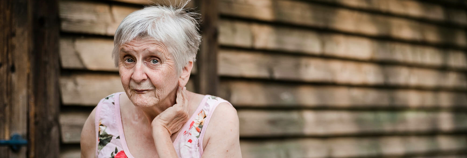 Alte Dame steht vor einer hölzenen Hütte