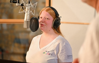 Eine Person bei der Gesangsaufnahme im Studio am Mikrofon