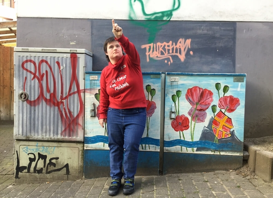 Junge Frau steht vor bemalten Kasten und zeigt mit dem Finger nach oben