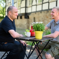 Bethel Regional Drevermannstift_Zwei Männer trinken lächelnd Kaffee sitzend an einem Tisch
