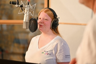 Eine Person bei der Gesangsaufnahme im Studio am Mikrofon