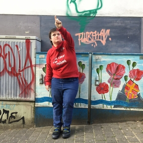 Junge Frau steht vor bemalten Kasten und zeigt mit dem Finger nach oben