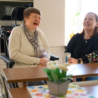 In Bethel Regional Haus am Lohbach in Dortmund sitzen zwei Frauen nebeneinander einer der Frauen sitzt auf einem Rollstuhl und sind zusammen am lachen