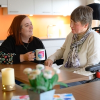 In Bethel Regional Haus am Lohbach in Dortmund sitzen zwei Frauen nebeneinander einer der Frauen sitzt auf einem Rollstuhl und sie unterhalten sich, eines der Frauen hält eine Tasse in der hand