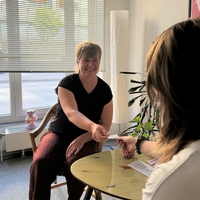 Zwei Frauen sitzen am Tisch der Frauenberatungsstelle von Bethel.regional. Eine Frau reicht der anderen eine Visitenkarte.