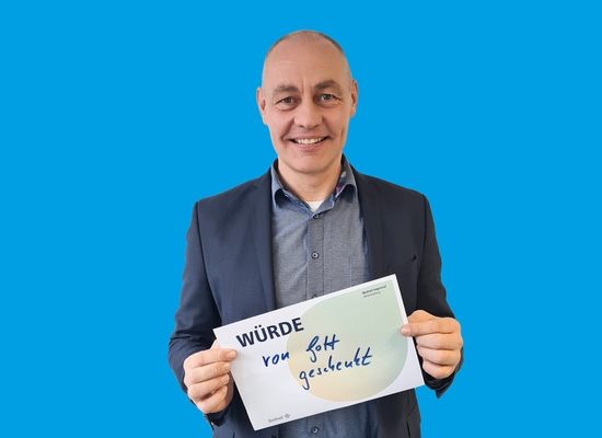 Man hält ein Schild in der Hand auf dem steht "Würde von Gott geschenkt"