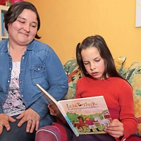 Eine Frau schaut einem Kind beim Lesen zu, Betreutes Wohnen in Familien