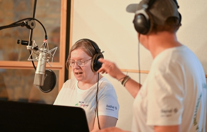 Zwei Personen bei der Gesangsaufnahme im Studio am Mikrofon